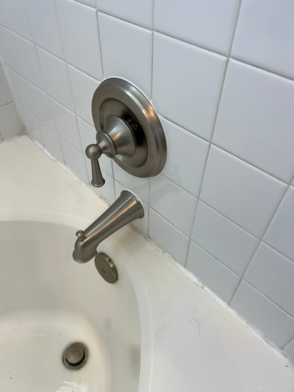 Brushed nickel bathtub faucet and spout installed on white tile surround