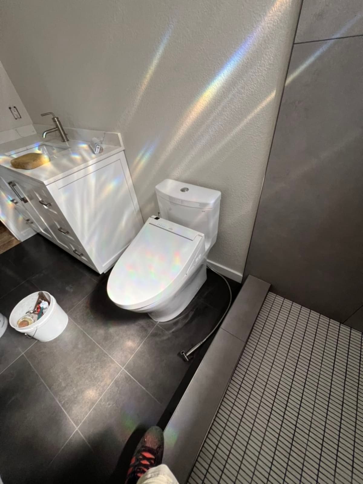 Modern bathroom with new elongated toilet, vanity, and dark tile floor